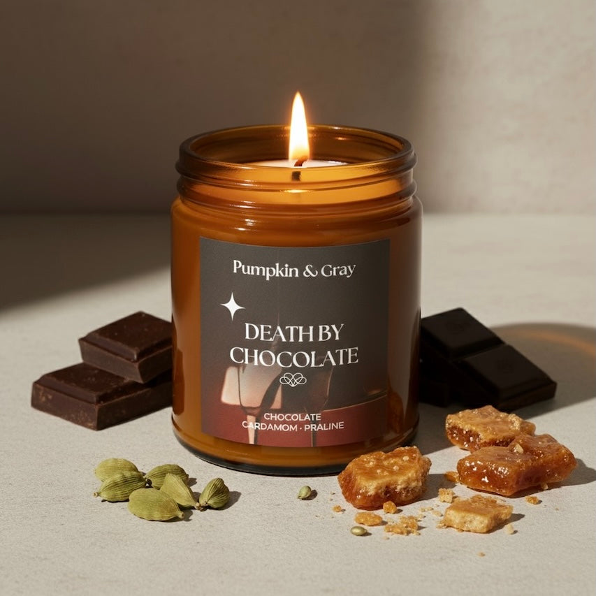 Candle in a jar labeled 'Death by Chocolate' by Pumpkin & Gray, surrounded by chocolate pieces and cardamom pods on a neutral background.