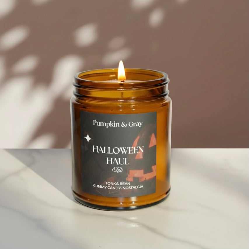 Candle in an amber jar labeled 'Pumpkin & Gray' with a Halloween theme on a neutral background.