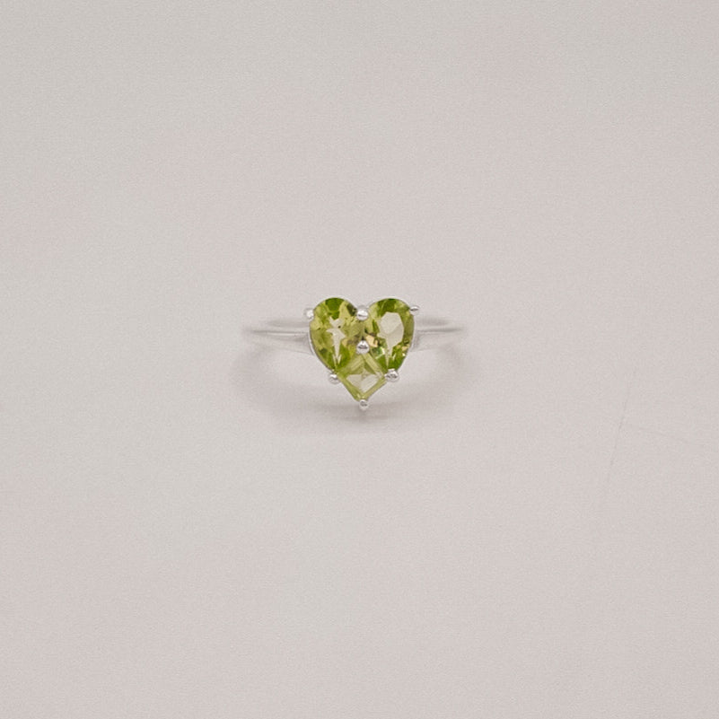 Heart-shaped green gemstone ring on a light gray background