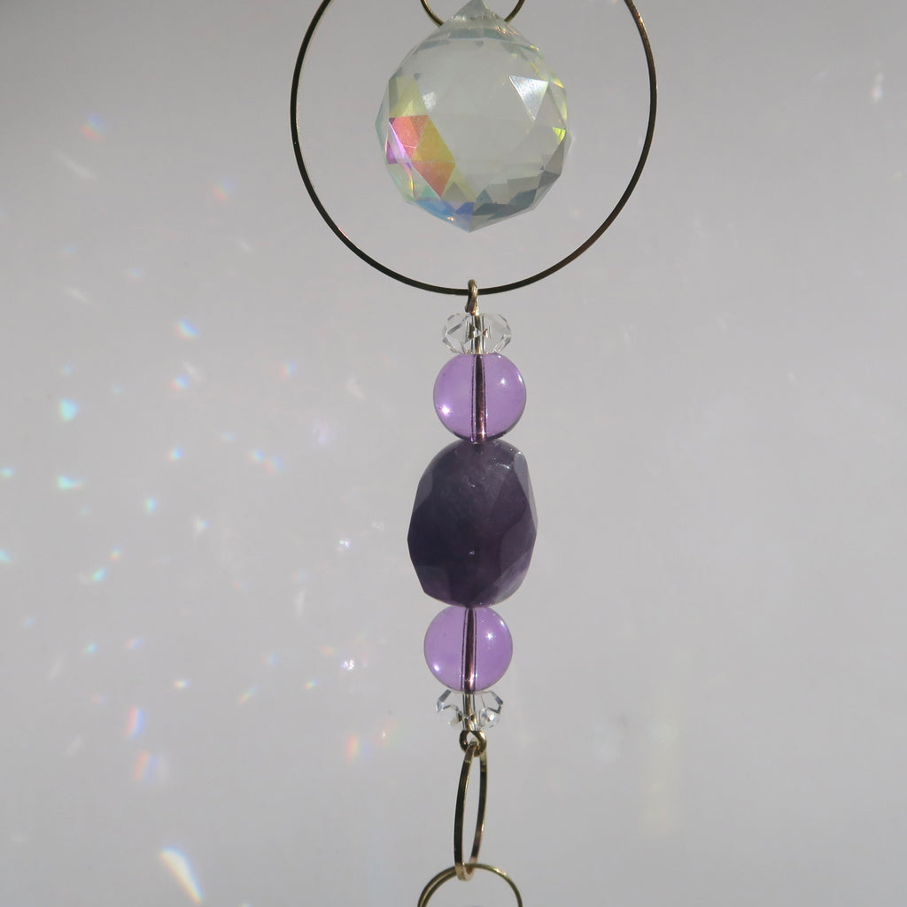 Decorative hanging with purple beads and a clear crystal on a light gray background