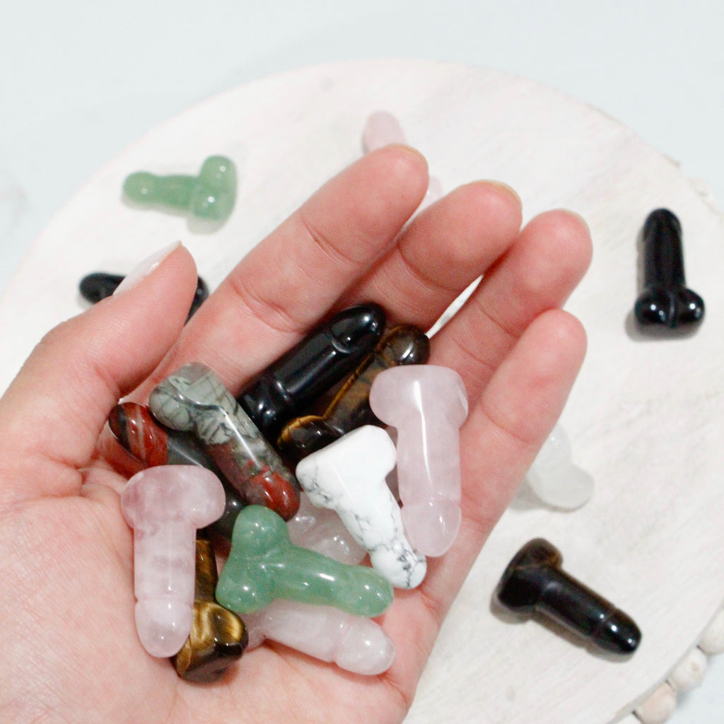 Handful of mini crystals shaped like penises in assorted crystals of rose quartz, clear quartz, howlite, aventurine, black obsidian, and tigers eye